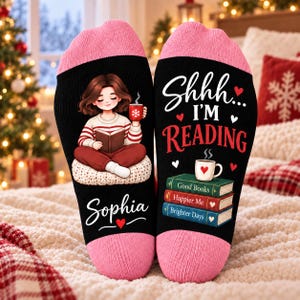 Può includere: Un paio di calzini neri con polsini rosa che raffigurano una persona che legge un libro con una tazza rossa. Il testo recita "Shhh... I'M READING" e "Sophia", con una pila di tre libri intitolati "Good Books", "Happier Me" e "Brighter Days".