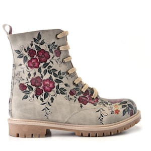 May include: A light gray combat boot with a floral design. The boot features a cream-colored sole, matching laces, and a pull tab. The floral pattern includes burgundy flowers and green leaves. The boot is a stylish and unique footwear option.