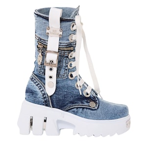 May include: A mid-calf denim boot featuring a white lace-up closure, a white vertical strap with a silver buckle, and a side zipper pocket. The boot has a thick, white, chunky platform sole with silver metallic accents and a square toe design.
