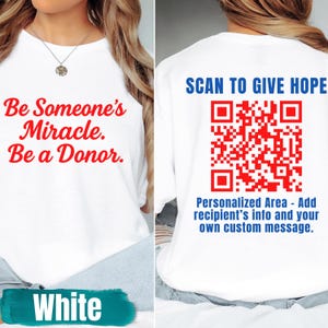 May include: White t-shirt with red text saying "Be Someone's Miracle. Be a Donor." The back of the shirt features a red QR code and the text "SCAN TO GIVE HOPE." Below the QR code is the text "Personalized Area - Add recipient's info and your own custom message."
