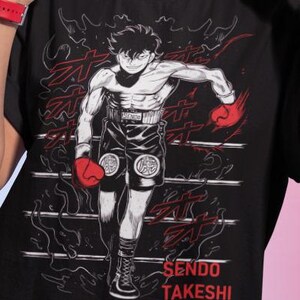 May include: Black t-shirt featuring a manga-style illustration of a boxer in a boxing ring. The design includes red boxing gloves, shorts, and the text "Sendo Takeshi". The shirt is a crew neck.