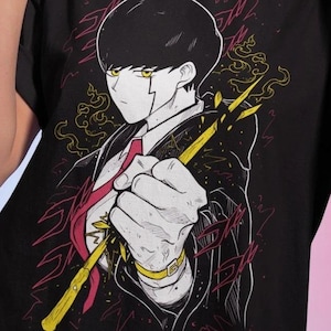 May include: Black t-shirt featuring a manga-style illustration of a character holding a yellow staff. The character has black hair, a white suit, and a red tie. The background has red and yellow accents.