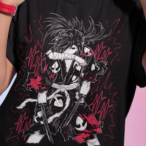 Puede incluir: Camiseta negra con un gr&aacute;fico de un personaje de anime con espadas, en rojo y blanco. La persona de la imagen lleva pendientes de aro dorados y un reloj rojo. El fondo tiene un degradado de rosa y azul.