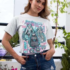 Puede incluir: Camiseta blanca con un gr&aacute;fico colorido de una cantante virtual con largo cabello turquesa. El dise&ntilde;o incluye texto japon&eacute;s y las palabras en ingl&eacute;s "Virtual Singer". Llevada por una persona en mezclilla azul.
