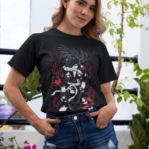 Puede incluir: Camiseta negra con un gr&aacute;fico detallado de un personaje con una espada, sobre un fondo de rayos rojos. El dise&ntilde;o es en negro, blanco y rojo. La modelo lleva una falda vaquera.