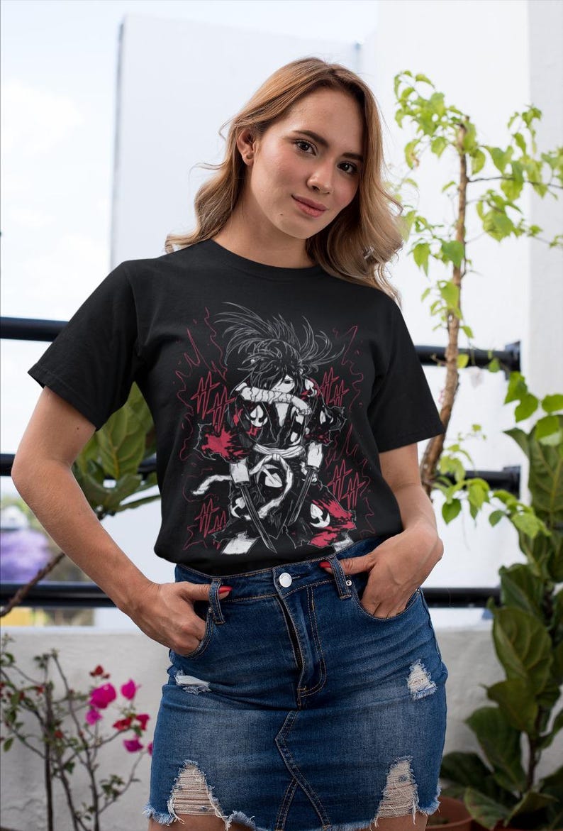 Puede incluir: Camiseta negra con un gr&aacute;fico detallado de un personaje con una espada, sobre un fondo de rayos rojos. El dise&ntilde;o es en negro, blanco y rojo. La modelo lleva una falda vaquera.