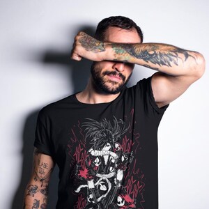 Puede incluir: Camiseta negra con una ilustraci&oacute;n detallada de estilo anime en rojo, negro y blanco. El gr&aacute;fico representa un personaje con pelo largo y una espada. La persona de la imagen tiene tatuajes en los brazos.