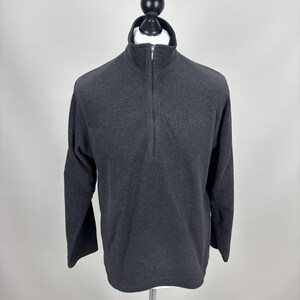 May include: A dark grey long-sleeved pullover shirt with a mock neck and a quarter-length zip. The shirt is displayed on a mannequin against a plain white background. The fabric appears to be a soft, knit material.