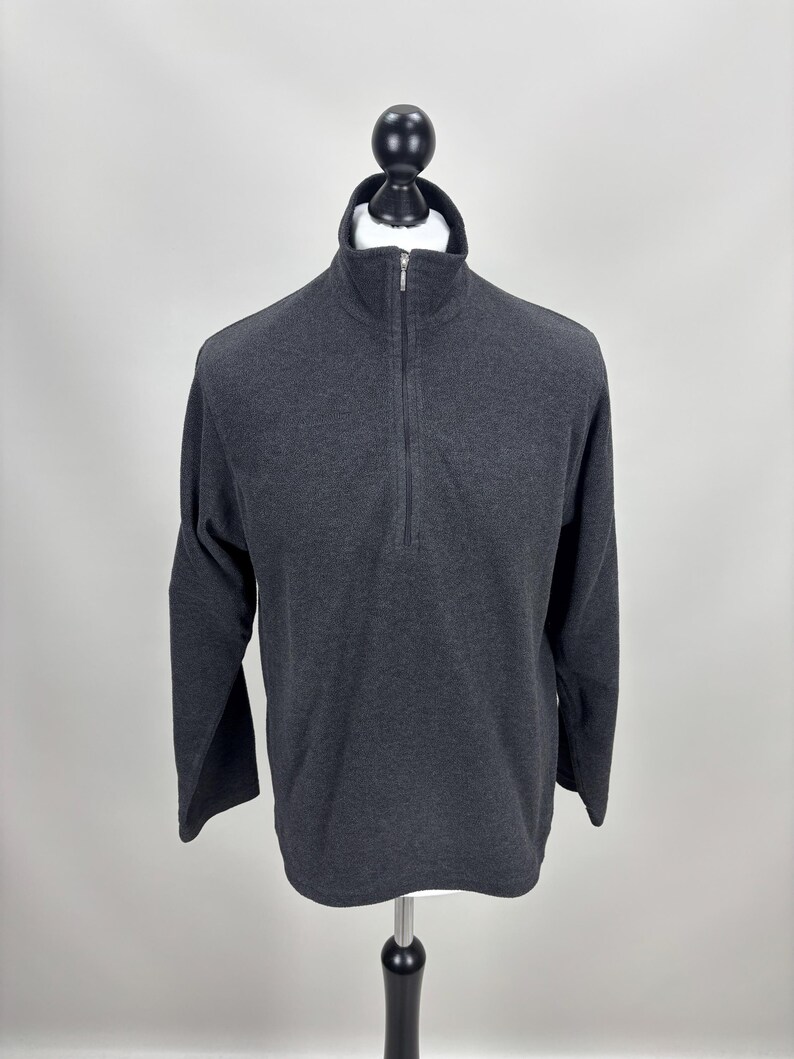 May include: A dark grey long-sleeved pullover shirt with a mock neck and a quarter-length zip. The shirt is displayed on a mannequin against a plain white background. The fabric appears to be a soft, knit material.