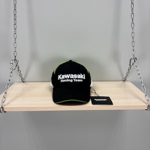 Puede incluir: Una gorra de béisbol negra con un borde verde lima en la visera y paneles laterales de malla. La parte frontal presenta el texto bordado en blanco Kawasaki Racing Team. Una etiqueta rectangular negra está sujeta al lateral de la gorra.