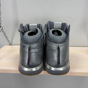 May include: A white ceramic mug with a black handle and the text "But First, Coffee" in a bold, black font. The mug is set against a blurred background, suggesting a cozy setting.