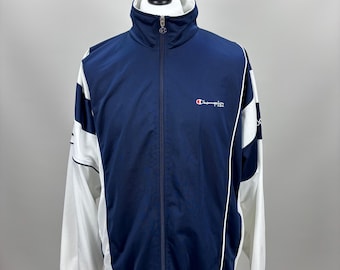 May include: A navy blue Champion track jacket with white accents. The jacket has a full zipper, a high collar, and the Champion logo on the chest. The sleeves are white with navy blue stripes.