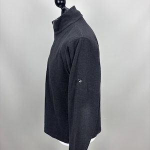 May include: A white ceramic mug with a black handle and the text "But First, Coffee" in a bold, black font. The mug is set against a blurred background, suggesting a cosy setting.