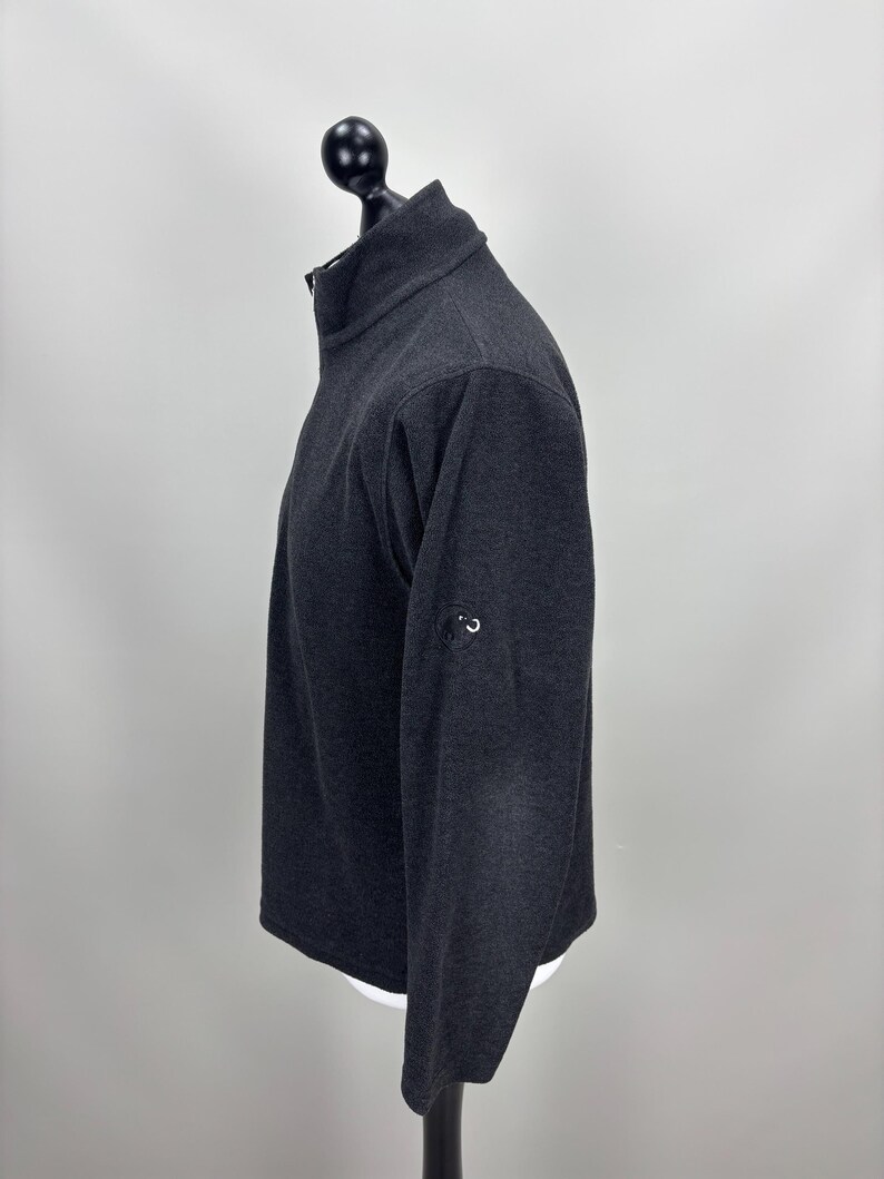 May include: A white ceramic mug with a black handle and the text "But First, Coffee" in a bold, black font. The mug is set against a blurred background, suggesting a cosy setting.