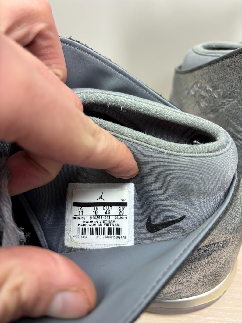 May include: Close-up of a gray and silver athletic shoe. The shoe's interior reveals a label with size information: US 11, UK 10, EUR 45, and 29 cm. The label also indicates the shoe was made in Vietnam.