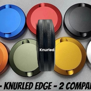 May include: A collection of colorful, round, blank, two-compartment containers with knurled edges. The containers are in various colors, including blue, red, black, orange, green, gold, and silver. The central piece is a black knurled edge with the word "Knurled".