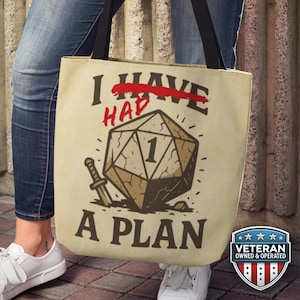 May include: Beige tote bag with black handles featuring a graphic of a D20 die with the text "I HAD A PLAN" in black and red. A sword is next to the die. A Veteran Owned & Operated badge is on the bottom right.