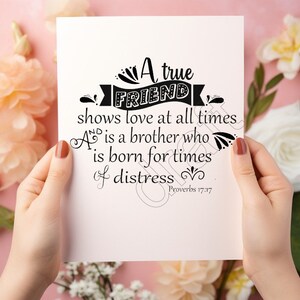 Può includere: Un biglietto bianco con testo nero che recita "Un vero AMICO dimostra amore in ogni momento. Un amico è un fratello che nasce per i momenti di difficoltà. Proverbi 17:17". Il biglietto è tenuto dalle mani di una persona.