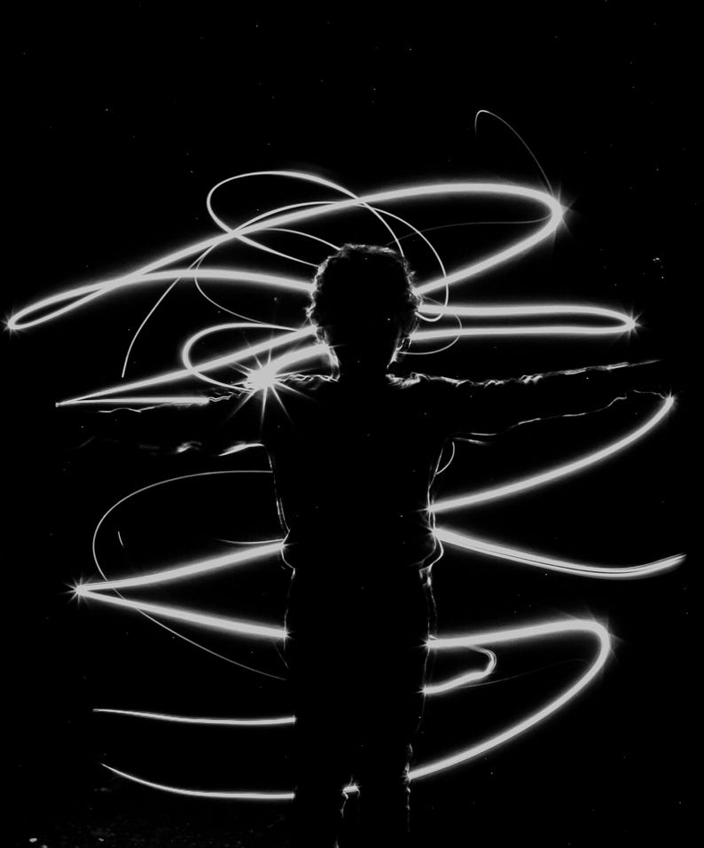 May include: A silhouette of a person with arms outstretched, surrounded by white light trails against a black background.