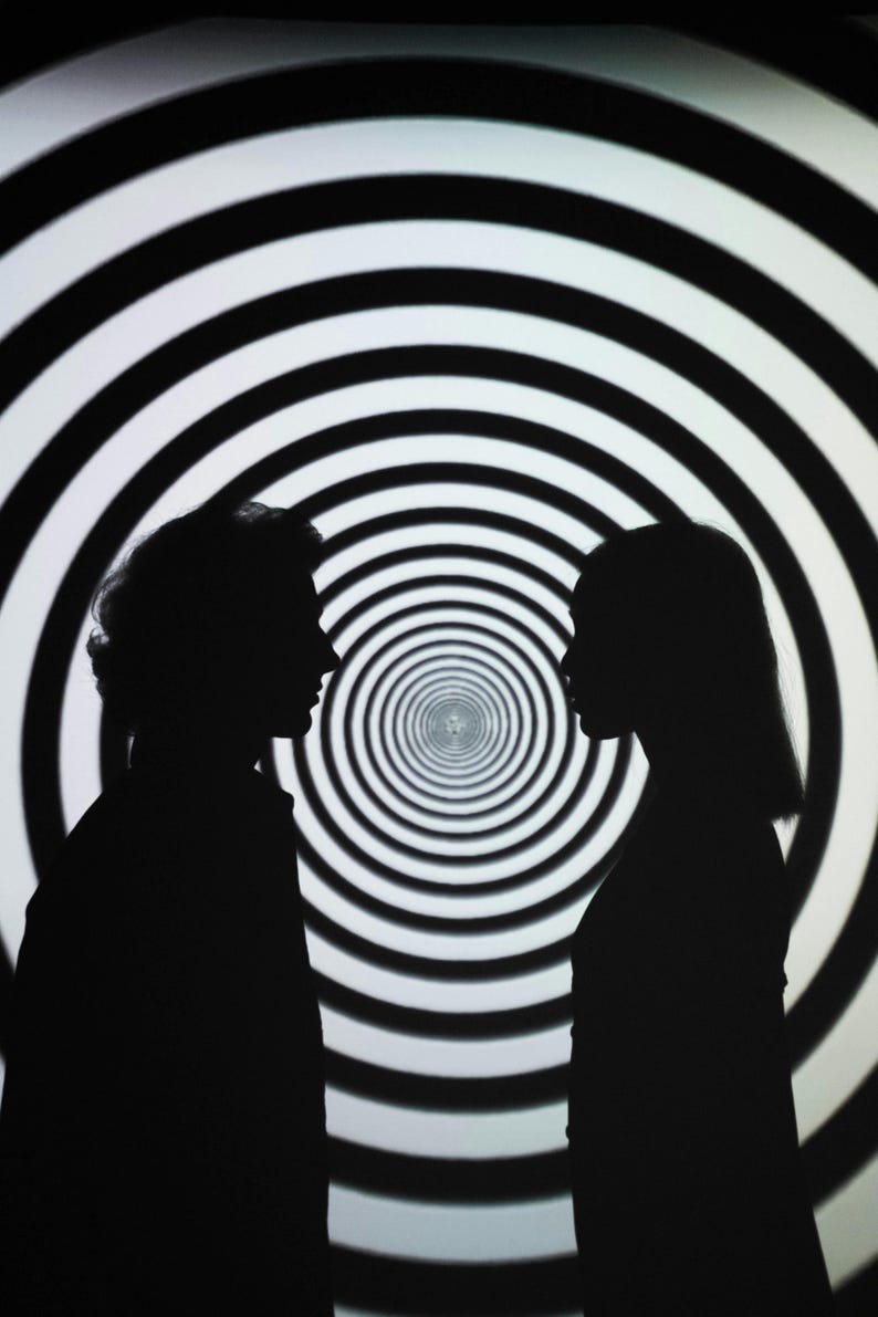 May include: Two silhouettes of people facing each other in front of a black and white swirling pattern.