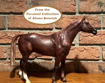 May include: A detailed brown horse figurine with a flowing mane and tail, posed in a standing position. The figurine has white accents on its legs and is set against a brick wall. Text on the image reads: "From the Personal Collection of Alison Bennish."