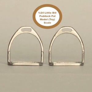 Puede incluir: Dos estribos plateados, uno al lado del otro, con una base rectangular y una parte superior curvada. El texto "1:24 Little Bit/ Paddock Pal Model (Toy) Scale" está en un círculo marrón encima de los estribos.