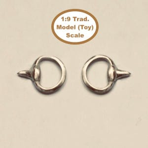 Op de afbeelding: Twee zilverkleurige modelpaardenbitjes. Elk bitje heeft een cirkelvormige ring en een uitstekende staaf. De afbeelding bevat de tekst "1:9 Trad. Model (Toy) Scale".
