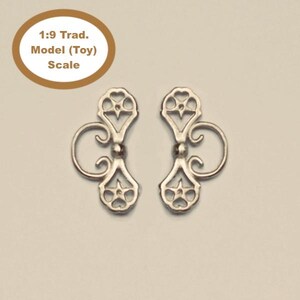 Op de afbeelding: Twee zilveren metalen decoratieve stukken met een bloemmotief. 1:9 Trad. Model (Speelgoed) Schaal.