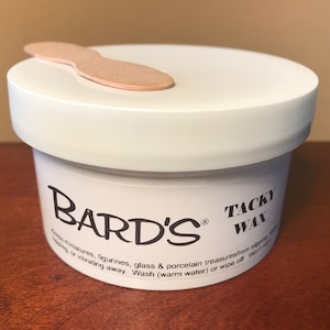 Peut inclure: Un pot en plastique blanc avec une étiquette noire qui indique "BARD'S" et "TACKY WAX". L'étiquette indique également "Keep miniatures, figurines, glass & porcelain treasures from slipping or vibrating away. Wash (warm water) or wipe off. Won't stain."