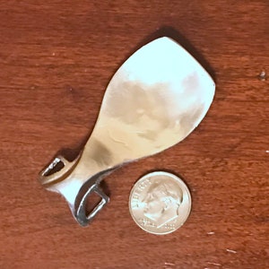 Op de afbeelding: Een zilverkleurige metalen sporen met een afgeronde, puntige punt en een decoratieve gesp. De sporen is ongeveer zo groot als een Nederlandse munt van tien cent.