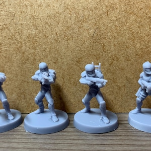 May include: Four gray plastic miniature figures of Star Wars clone troopers, each holding a blaster rifle and standing on a gray plastic base.