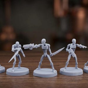 May include: Five gray miniature figurines of futuristic soldiers, each posed differently. They are standing on circular bases and holding weapons, including rifles and a sword. The figures are set against a blurred background.
