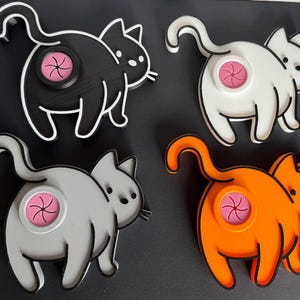 May include: Four ceramic cat figurines with different coloured bodies, black, white, grey, and orange. Each cat has a pink swirl design on its backside.