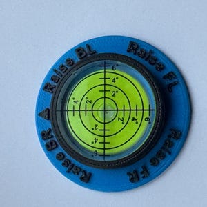 A circular level with a black rim and a blue outer ring. The level has a green bubble level with black markings. The text 'Raise BL' and 'Raise FL' are printed on the outer ring.