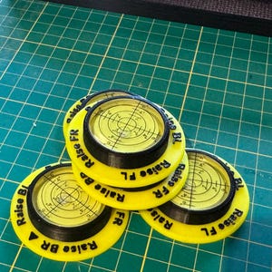 May include: Three circular yellow and black spirit level tools with clear liquid-filled centres featuring crosshair markings. Each unit has black text printed on the yellow rim that reads Raise FR, Raise FL, Raise BR, and Raise BL in various orientations.