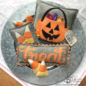 May include: A set of felt Halloween decorations on a silver platter. The decorations include a pumpkin-shaped bag with the words "Trick or Treat Candy" on a tag, a pillow with the word "Treat" on it, and several candy corn shapes.