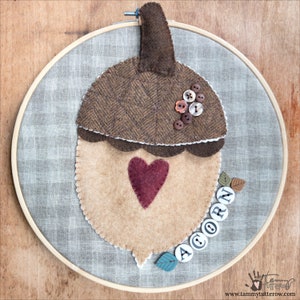 May include: A brown and tan felt acorn with a heart in the centre and the word "ACORN" spelled out with buttons. The acorn is hanging from a hoop.