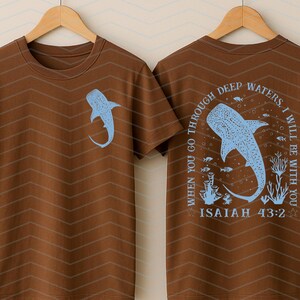 May include: Brown t-shirt with a light blue whale shark graphic on the front and back. The back of the shirt features the text "WHEN YOU GO THROUGH DEEP WATERS, I WILL BE WITH YOU" and "ISAIAH 43:2". The shirt has a chevron pattern.