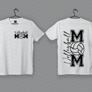 May include: Two white t-shirts with a black graphic. One says "Volleyball Mom" with a volleyball, the other has "Volleyball" vertically with "MOM" and a volleyball with a heart.