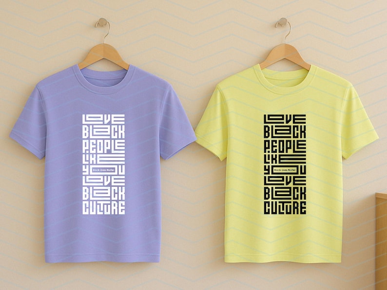 May include: Two short-sleeved t-shirts, one lavender and one yellow, hang on wooden hangers. Each shirt features the text "LOVE BLACK PEOPLE LIKE YOU LOVE BLACK CULTURE" in a vertical, blocky design. The text is white on the lavender shirt and black on the yellow shirt.