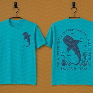 May include: Teal t-shirt with a shark graphic on the front and back. The front features a shark silhouette. The back displays a larger shark design with the text "When you go through deep waters, I will be with you. Isaiah 43:2."