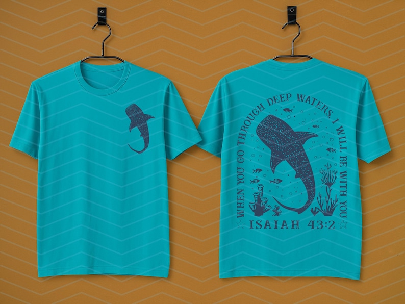 May include: Teal t-shirt with a shark graphic on the front and back. The front features a shark silhouette. The back displays a larger shark design with the text "When you go through deep waters, I will be with you. Isaiah 43:2."