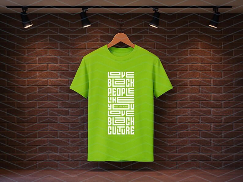 May include: A lime green t-shirt with the text "LOVE BLACK PEOPLE LIKE YOU LOVE BLACK CULTURE" in white block letters. The shirt is hanging on a wooden hanger against a brick wall.