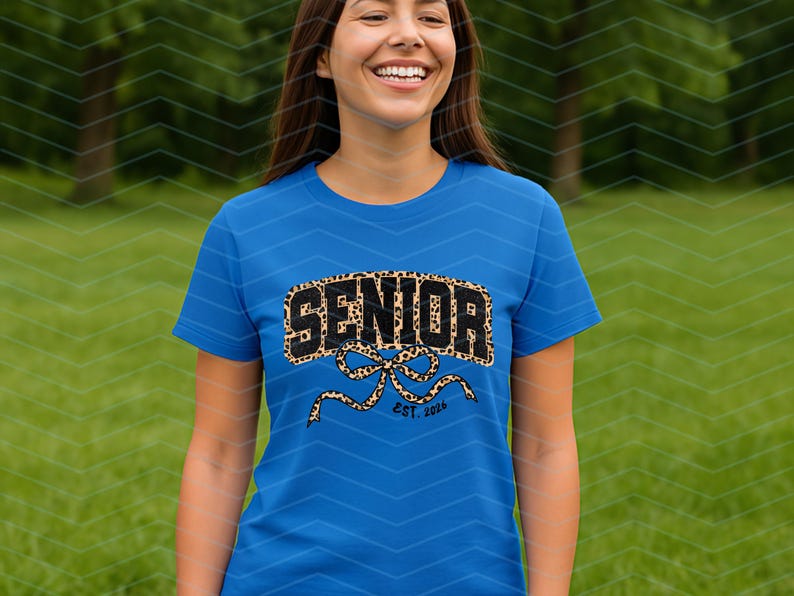 May include: A blue t-shirt with the word "SENIOR" in a leopard print design. Below the word "SENIOR" is a bow design with the text "EST. 2024". The shirt is worn by a person in a green outdoor setting.