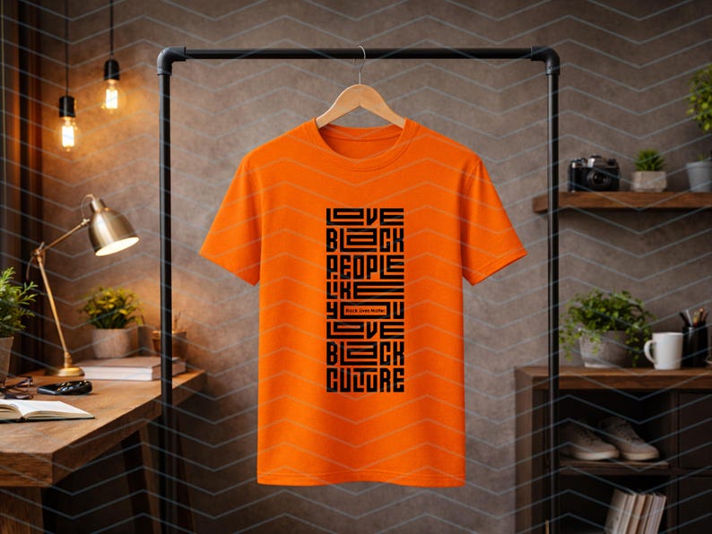May include: An orange t-shirt with the text "Love Black People Like You Love Black Culture" in black, displayed on a black clothing rack. The shirt is hanging on a wooden hanger.