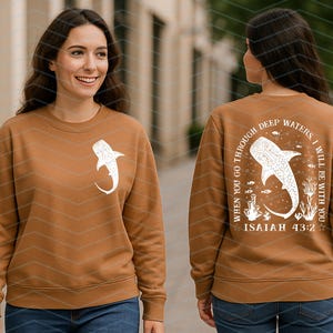 May include: A brown sweatshirt with a white whale shark graphic on the front and back. The back of the sweatshirt has the text "WHEN YOU GO THROUGH DEEP WATERS, I WILL BE WITH YOU" and "ISAIAH 43:2".