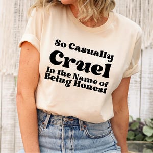 May include: A white t-shirt with black text that reads "So Casually Cruel In the Name of Being Honest".
