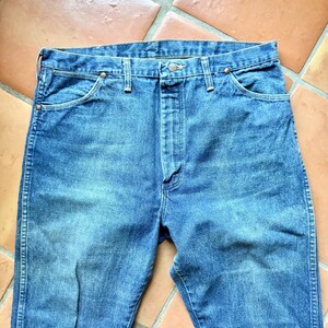 May include: Blue denim jeans with a classic five-pocket design. The jeans have a button and zipper closure, along with copper-colored rivets. The fabric shows signs of wear, suggesting a vintage or well-loved item.
