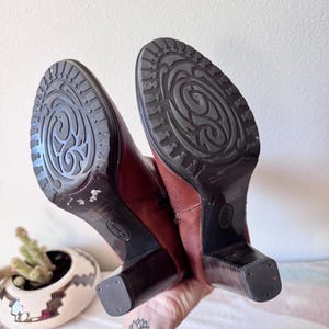 May include: A handmade wooden sign with the text "Welcome to our home" in a handwritten style. The sign is painted white with a distressed finish and features a dark brown border. A small, decorative heart is attached to the bottom.