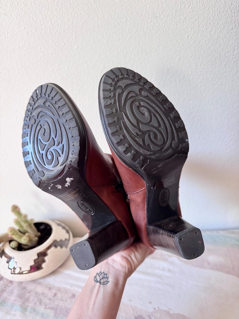 May include: A handmade wooden sign with the text "Welcome to our home" in a handwritten style. The sign is painted white with a distressed finish and features a dark brown border. A small, decorative heart is attached to the bottom.